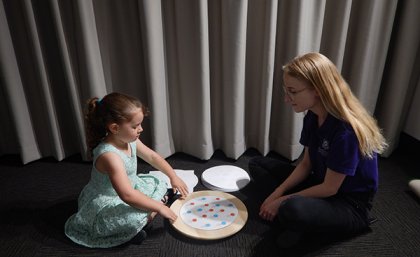 Young girl sitting with UQ PhD candidate manually rotating a turntable